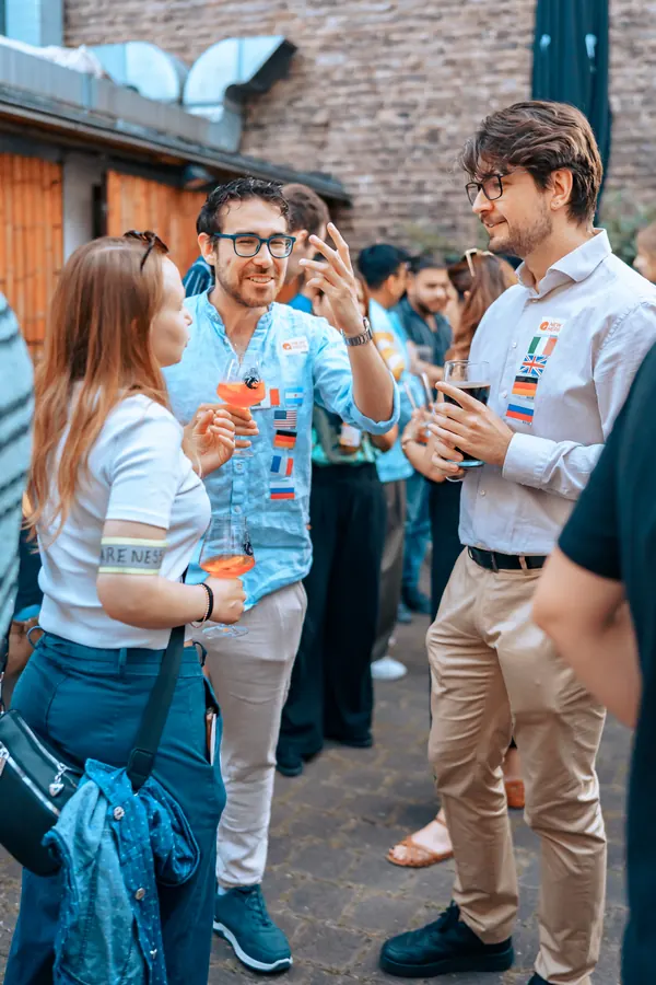 Guests with language flag stickers talking in the courtyard at °Plato Beer & BBQ at the social in Bonn