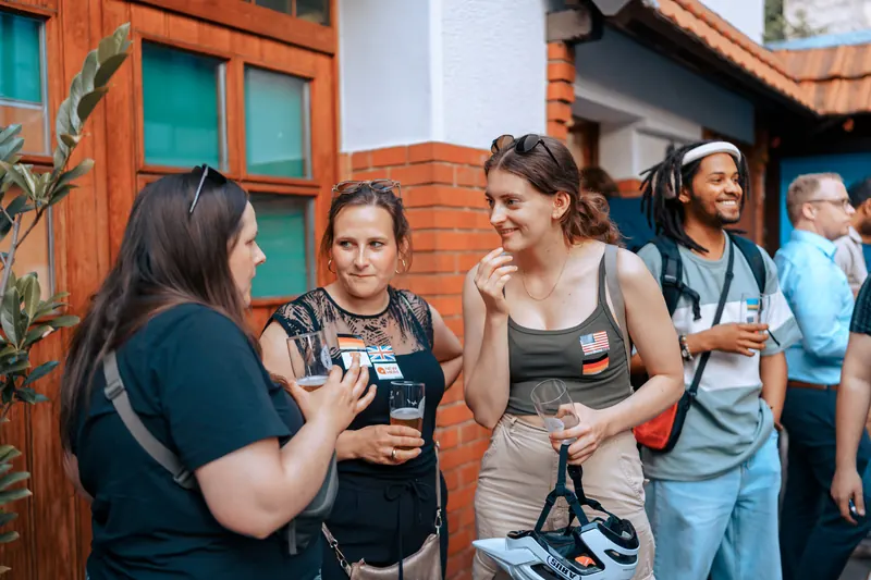 Guests with language flag stickers laughing together in the courtyard at °Plato Beer & BBQ in Bonn