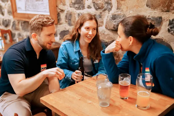 Three guests laughing over drinks at a wooden table at the SMP social at °Plato Beer & BBQ in Bonn