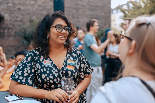 A guest with a flag sticker smiling in conversation in the courtyard at the Thursday social in Bonn