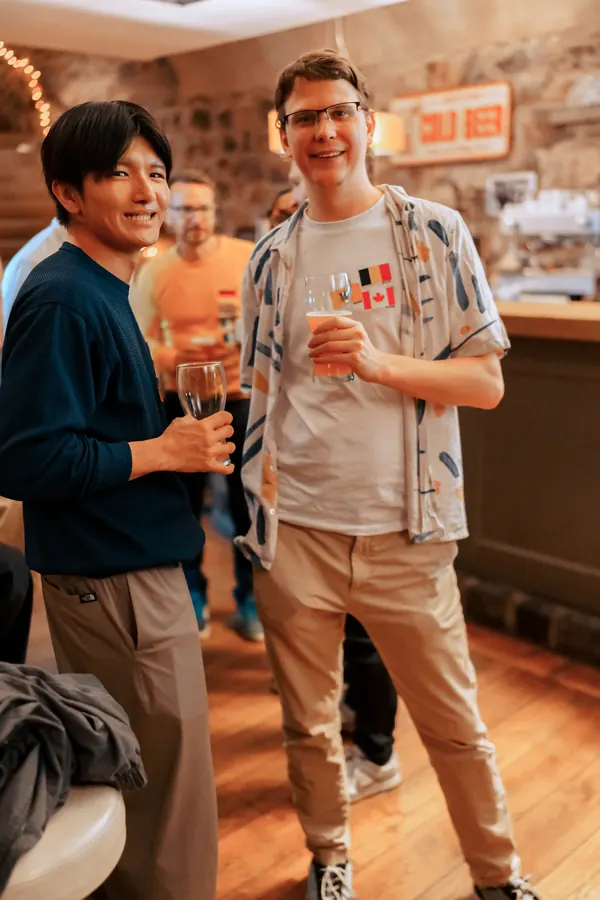 Two guests with language flag stickers smiling at the bar inside °Plato Beer & BBQ in Bonn