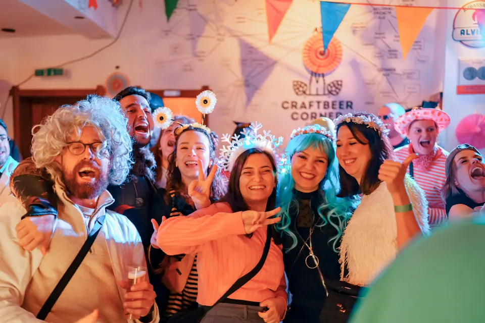 A big group in carnival costumes cheering in front of the Craftbeer Corner wall