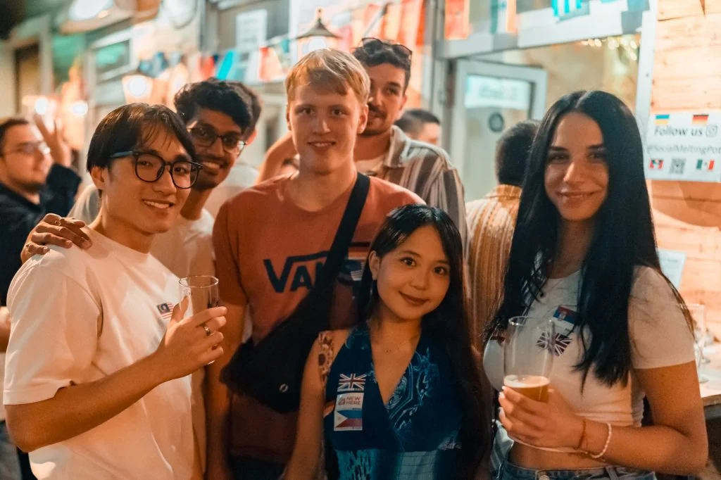 Six guests with language flag stickers smiling together inside Craftbeer Corner Coeln at the Wednesday social in Cologne