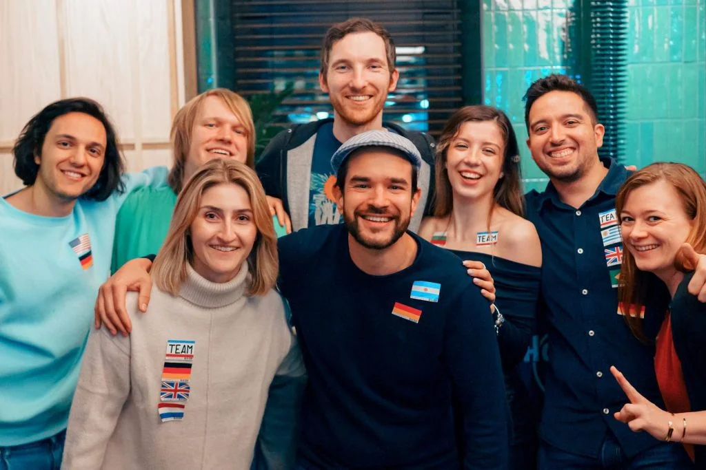 A group of internationals with language flag stickers smiling arm in arm at a Social Melting Pot night in Cologne