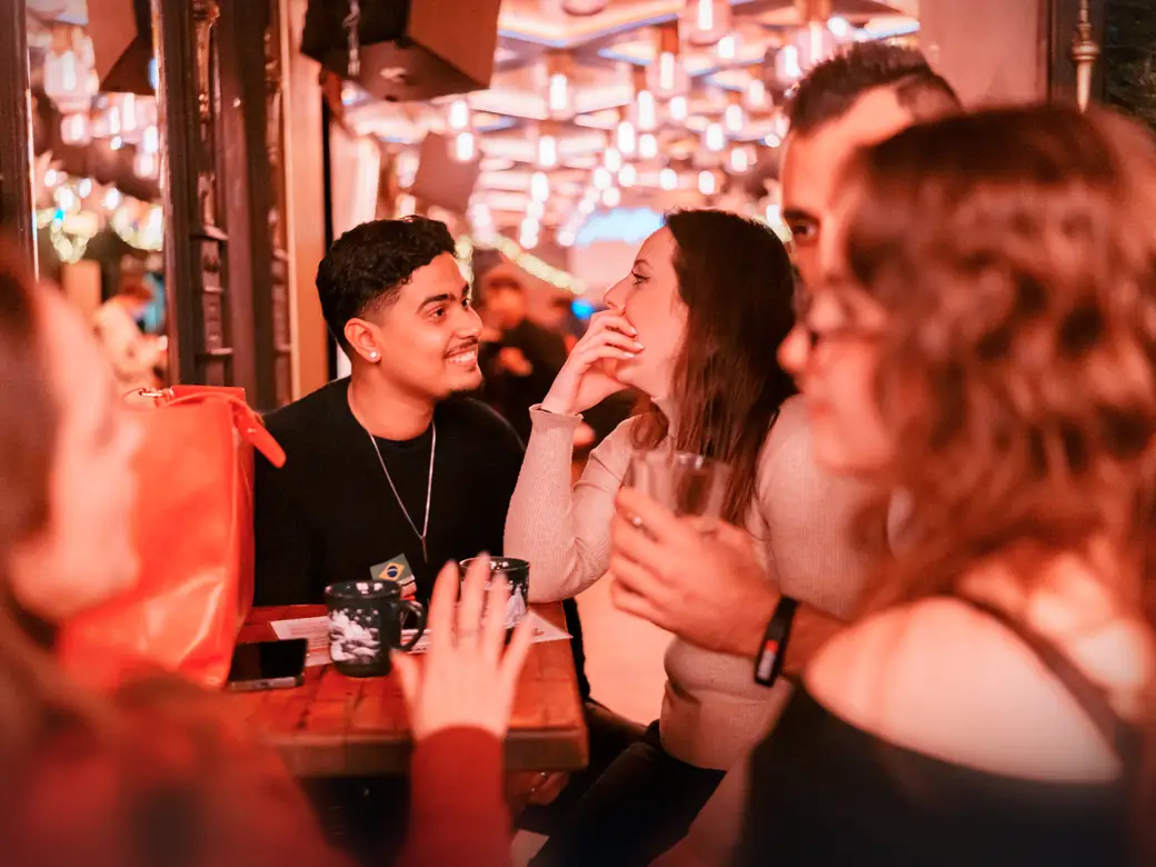 A guy and a woman laugh together at a table over drinks on a night at Goldfinger in Cologne