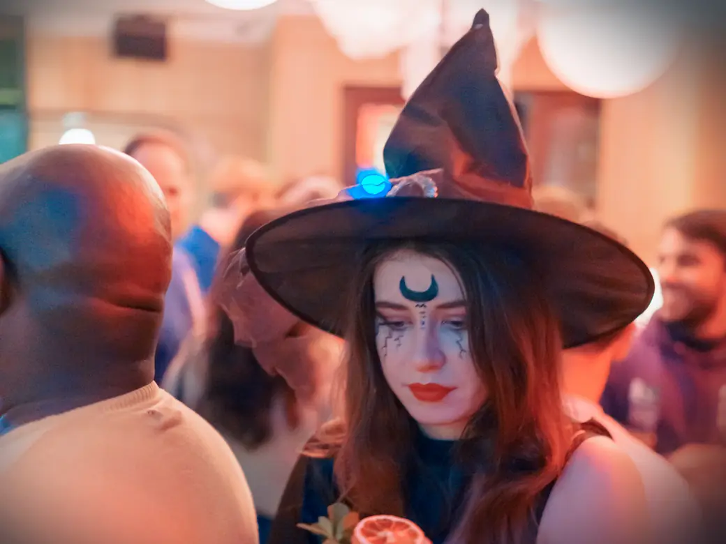 A guest in a witch hat with a painted moon on her forehead at a Social Melting Pot Halloween party in Cologne