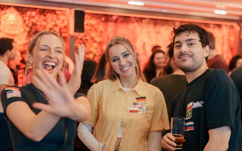 Three guests with language flag stickers laughing at the Wednesday social at Craftbeer Corner Coeln in Cologne