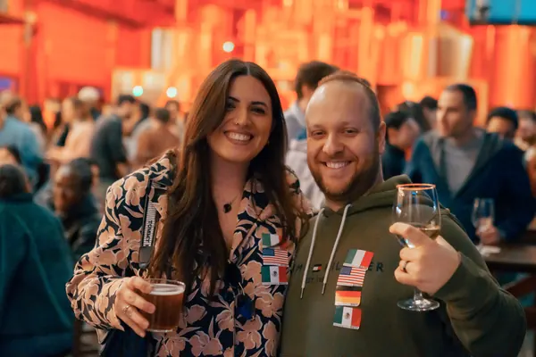 Two guests with language flag stickers smiling with drinks inside Brauerei Kürzer at the social in Düsseldorf