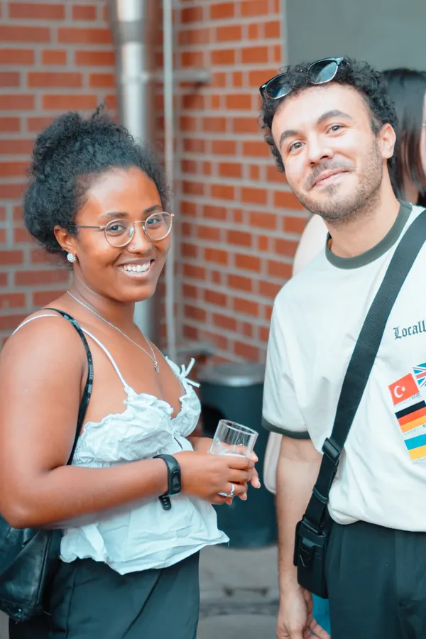 Two guests with language flag stickers smiling at the SMP social outside Brauerei Kürzer in Düsseldorf