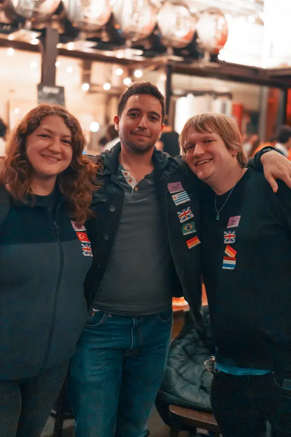 Three guests with language flag stickers arm in arm at the Social Melting Pot social in Düsseldorf