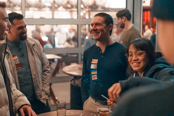 Three guests with flag stickers laughing together at a standing table at Brauerei Kürzer in Düsseldorf
