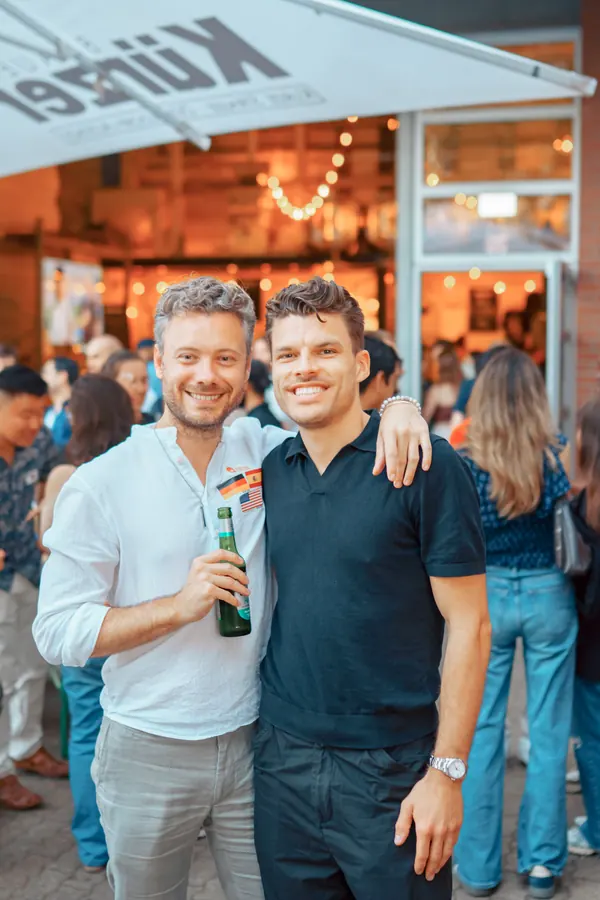Two friends arm in arm with drinks under the Kürzer sign at a Social Melting Pot night in Düsseldorf