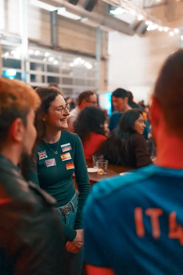 A guest with flag stickers laughing in a group inside Brauerei Kürzer at the social in Düsseldorf