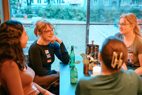 Guests with flag stickers chatting at a window table inside Bar Grüner Jäger at the social in Hamburg