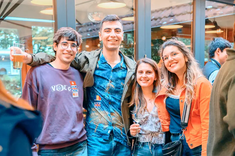 Four guests with language flag stickers smiling arm in arm at the Social Melting Pot social in Hamburg